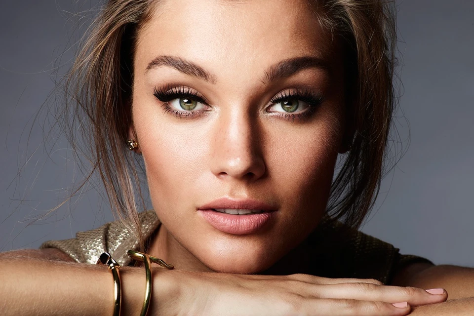 Close-up portrait of a woman with green eyes and gold bracelets against a gray backdrop, with focus on beauty and fashion.