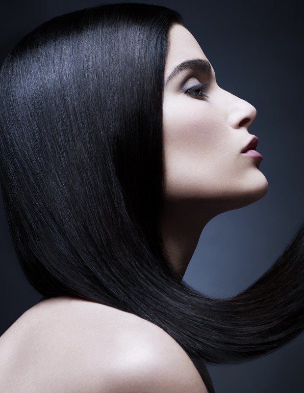 Profile view of a woman with long, dark, sleek hair cascading over her shoulder, against a dark gray background, studio lighting.