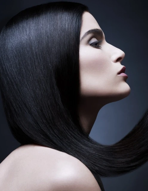 Profile view of a woman with long, dark, sleek hair cascading over her shoulder, against a dark gray background, studio lighting.