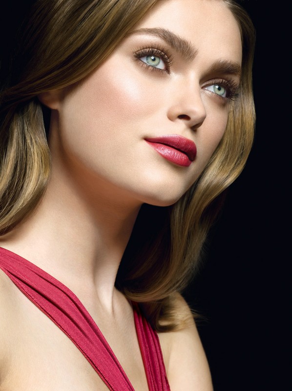 A close-up studio shot of a blonde woman with red lipstick and a red dress against a dark backdrop, showcasing a beauty and fashion aesthetic.