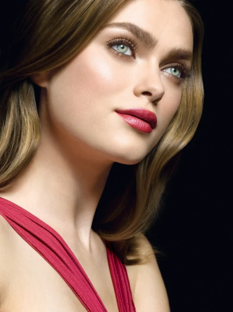 A close-up studio shot of a blonde woman with red lipstick and a red dress against a dark backdrop, showcasing a beauty and fashion aesthetic.