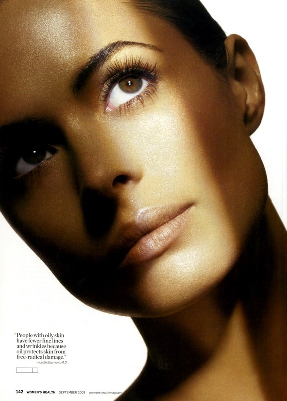 Close-up beauty shot of a woman with tan skin looking up and slightly tilted, with a shadow on her face and a white background.
