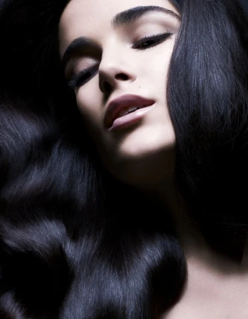 Glamorous portrait of an adult woman with dark hair and makeup. The image highlights the beauty and elegance against a dark backdrop.