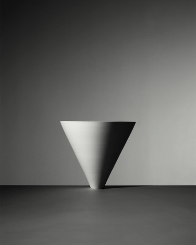 Monochromatic still life of a minimalist white cone placed on a gray surface against a gradient gray backdrop, creating a serene aesthetic.