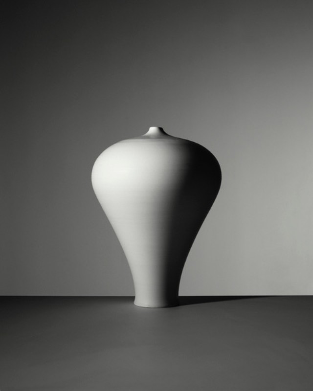 Monochrome still life: a studio shot of a modern white ceramic vase with a rounded body and narrow neck, set against a gray background.
