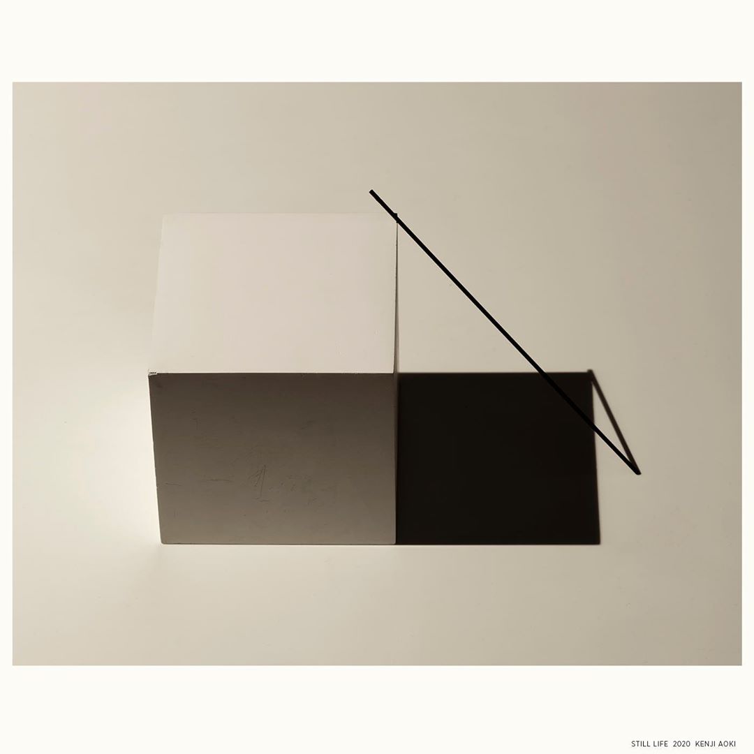 Minimalist still life art featuring geometric shapes in shades of white, gray, and black, divided by a black line on an off-white background.