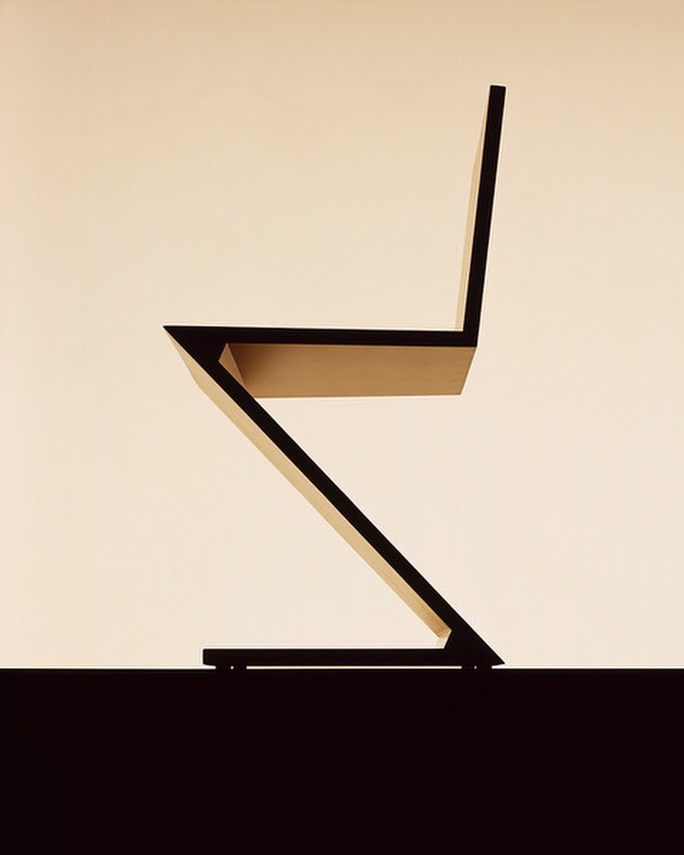 Zig-zag chair in black with a minimalist aesthetic on a pale tan background, showcasing its unique shape and design.