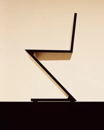 Minimalist side profile of a modern angular wooden chair against a warm neutral gradient background.