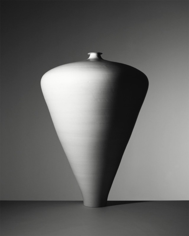Monochrome studio shot of a large, cone-shaped ceramic vase with a narrow neck, set against a gradient gray background, showcasing simple elegance.