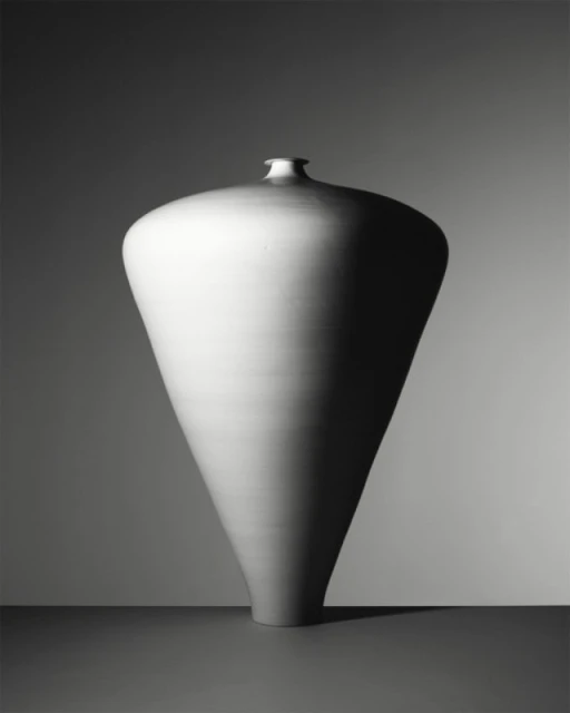 Monochrome studio shot of a large, cone-shaped ceramic vase with a narrow neck, set against a gradient gray background, showcasing simple elegance.