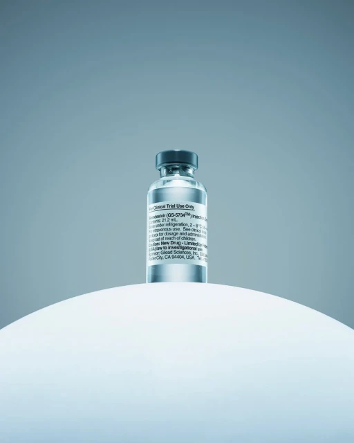 A close-up showcases a vial of Remdesivir atop a white, rounded surface against a soft, gradient blue backdrop, emphasizing its pharmaceutical nature.