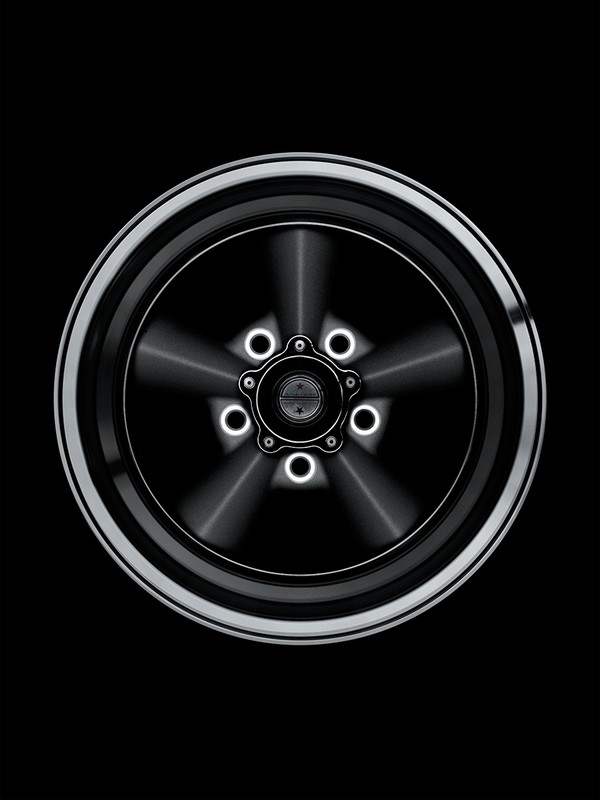 Close-up of a stylized silver and black car wheel with a five-star center design against a dark background, automotive design.