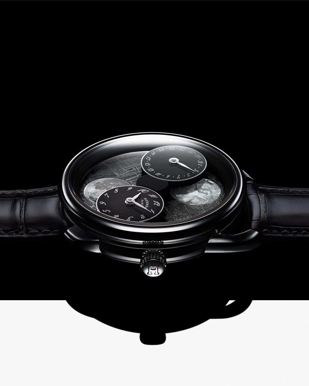 Close-up studio shot of an elegant black wristwatch with leather band, black watch face, and silver details, against black and white background.