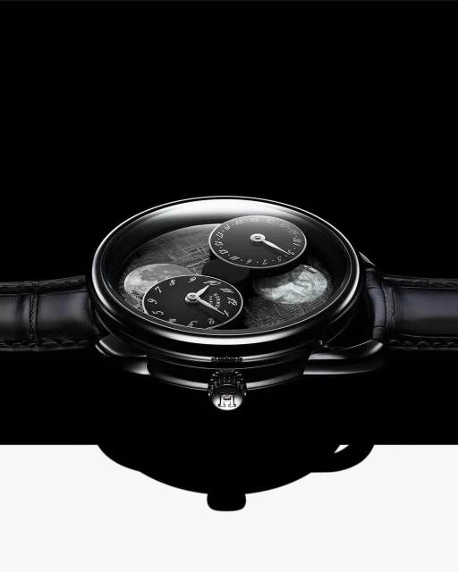 Close-up studio shot of an elegant black wristwatch with leather band, black watch face, and silver details, against black and white background.