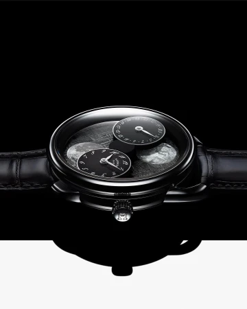 Close-up studio shot of an elegant black wristwatch with leather band, black watch face, and silver details, against black and white background.
