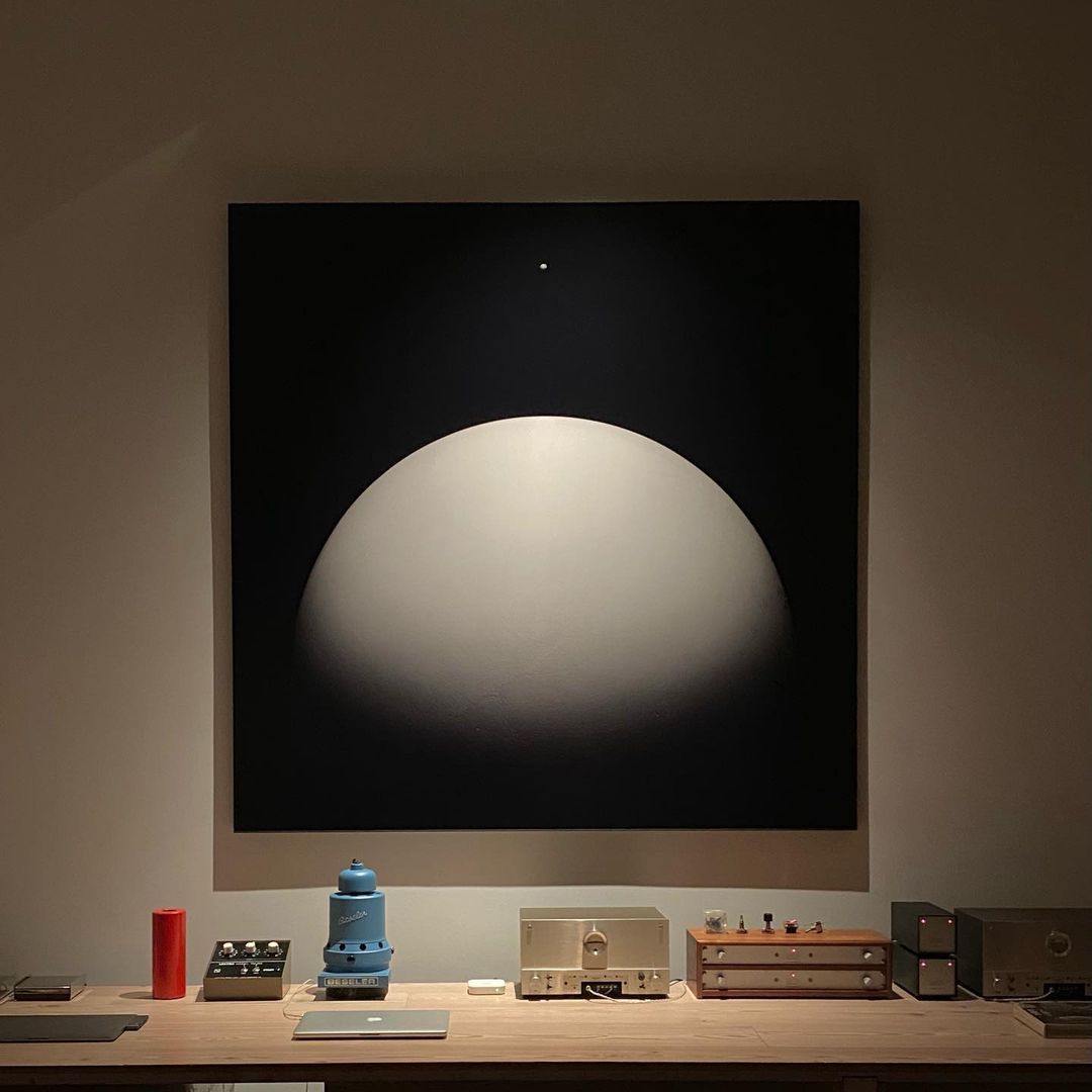 Abstract black and white painting above a wooden table with retro-style audio equipment in a dimly lit, neutral-toned room.