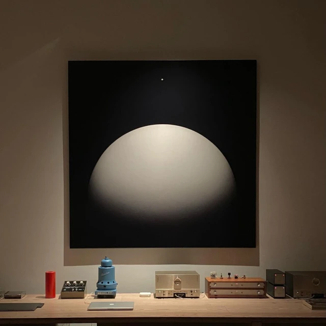 Abstract black and white painting above a wooden table with retro-style audio equipment in a dimly lit, neutral-toned room.