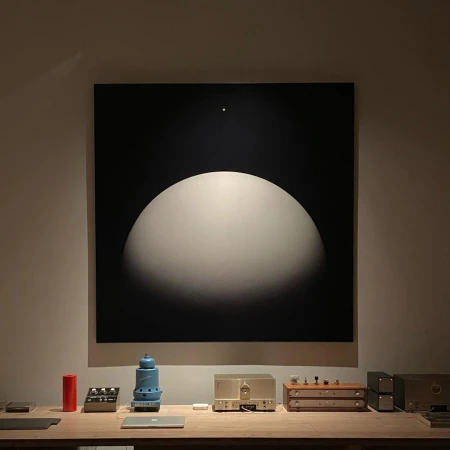 Abstract black and white painting above a wooden table with retro-style audio equipment in a dimly lit, neutral-toned room.
