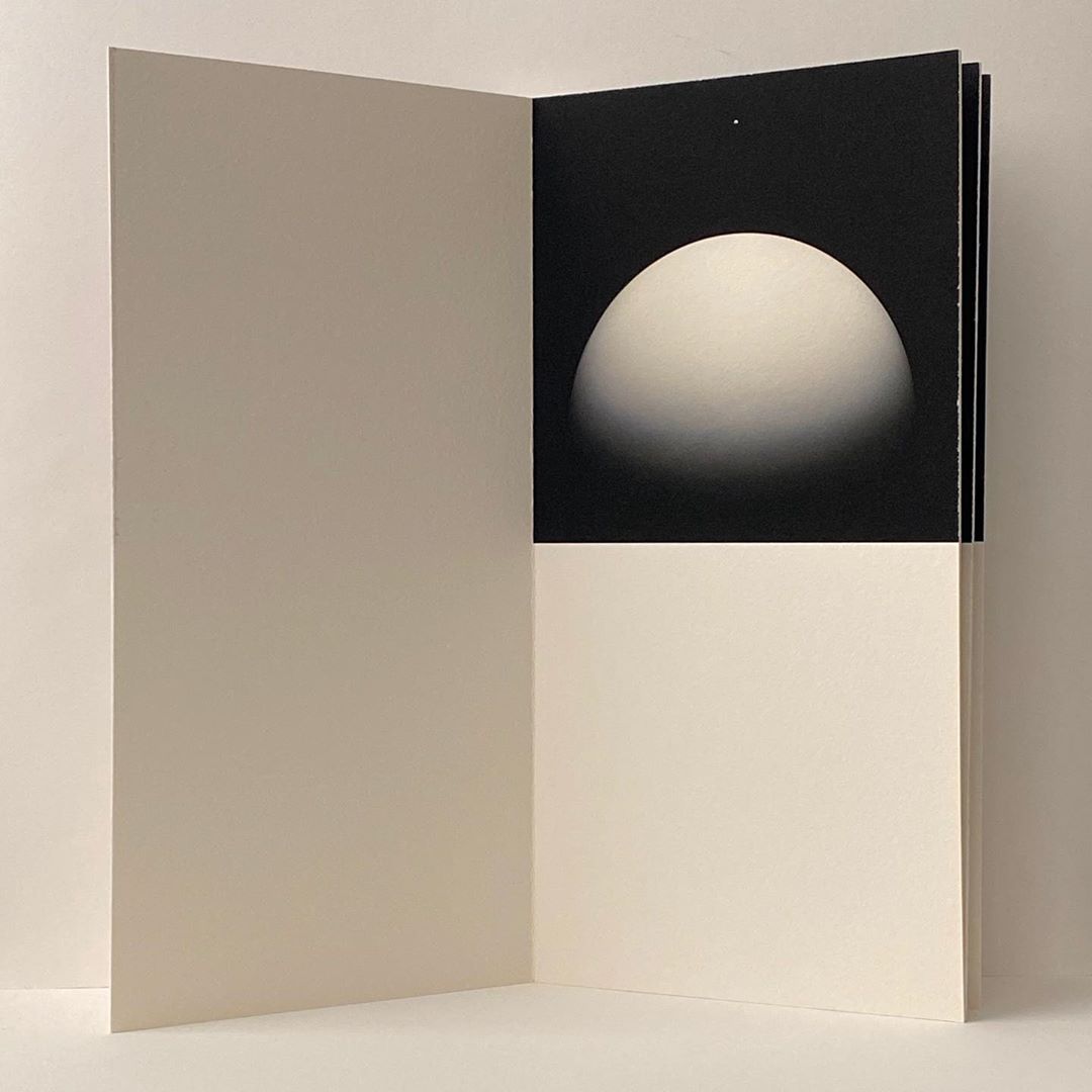An open book with a spherical graphic, presented on white paper, exhibiting a minimalistic yet visually striking aesthetic.