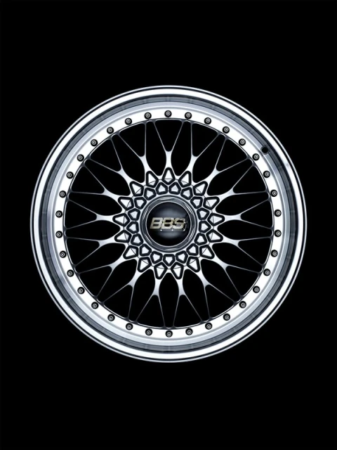 Detailed shot of a silver multi-spoke BBS wheel rim with a black center cap, captured in a dark, high-contrast studio setting.
