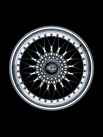 Detailed shot of a silver multi-spoke BBS wheel rim with a black center cap, captured in a dark, high-contrast studio setting.