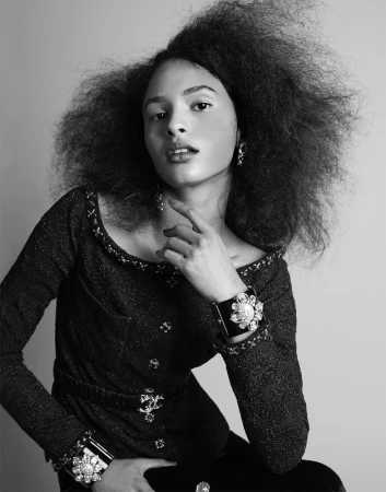 Black and white portrait of a woman with voluminous textured hair wearing a patterned tweed jacket and jeweled cuffs