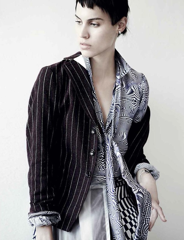 Model with dark short hair wearing a pinstripe blazer and patterned shirt against a plain white background