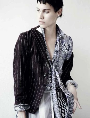 Model with dark short hair wearing a pinstripe blazer and patterned shirt against a plain white background