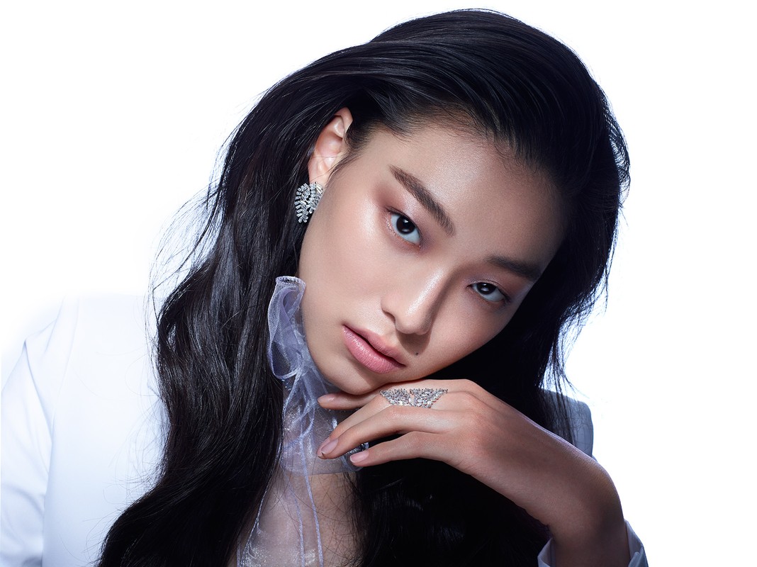 Close-up of a stylish Asian female model with black hair wearing diamond earrings and ring against a bright white backdrop.