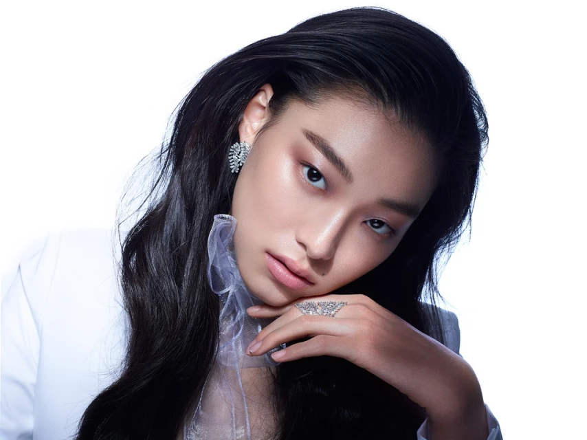 Close-up of a stylish Asian female model with black hair wearing diamond earrings and ring against a bright white backdrop.