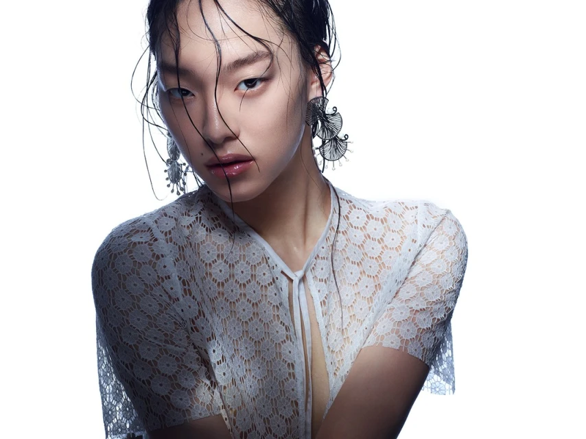 Headshot of Asian woman with wet hair and large earrings, wearing a lace top against a bright white backdrop in a portrait-style image.