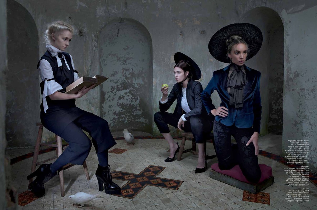 Editorial fashion shoot in an aged interior features three female models in stylish dark suits, black hats and white doves. 