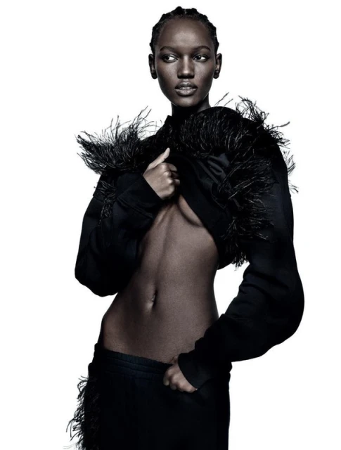 Elegant studio shot of a slender Black woman in a cropped feathered jacket and matching skirt against a pure white background.