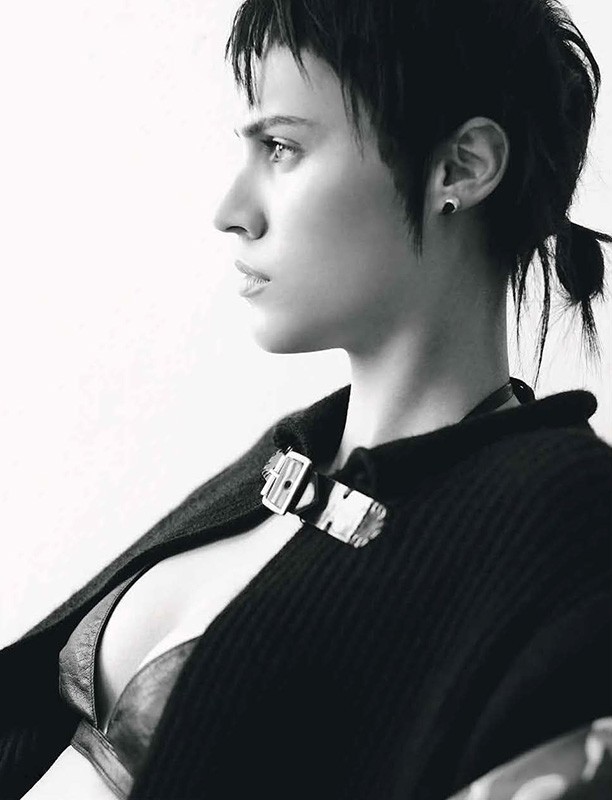 Black and white portrait of a woman in profile with short dark hair, wearing a dark open sweater and a visible bra-like top.