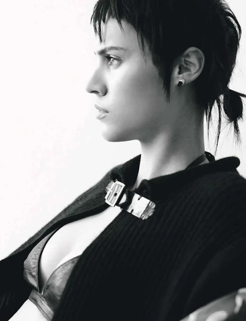 Black and white portrait of a woman in profile with short dark hair, wearing a dark open sweater and a visible bra-like top.