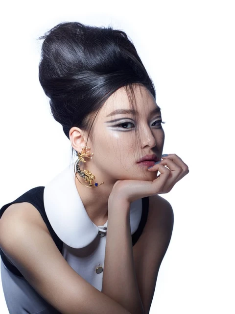 Close-up studio shot of an Asian woman with dramatic eye makeup, bouffant hairstyle, ornate earrings, and a vintage-style collar.