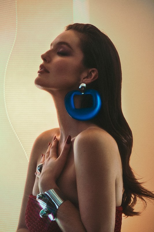 Profile portrait of a woman with long dark hair wearing large blue hoop earrings and a silver cuff bracelet.