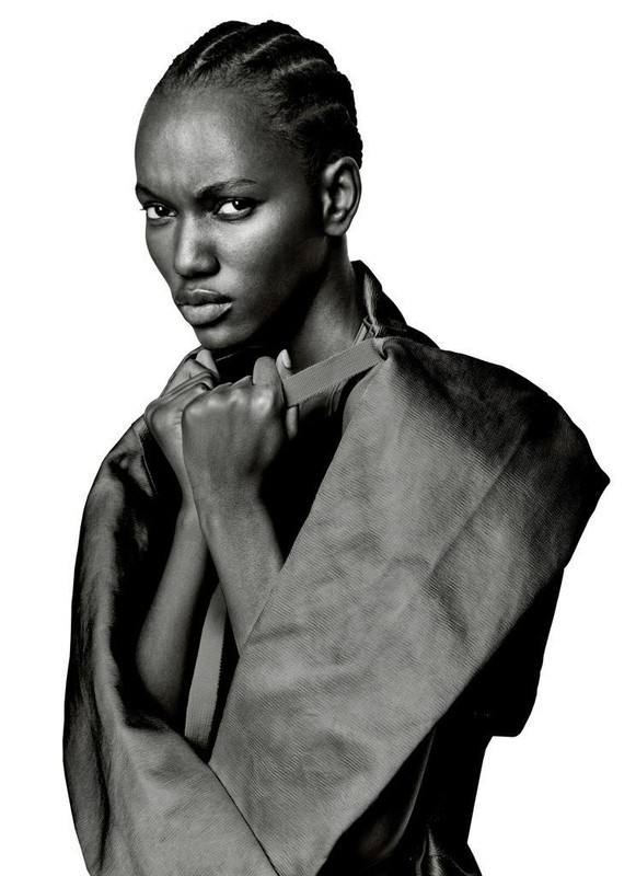 Black-and-white portrait of a woman with braided hair wearing a dark structured garment against a white background