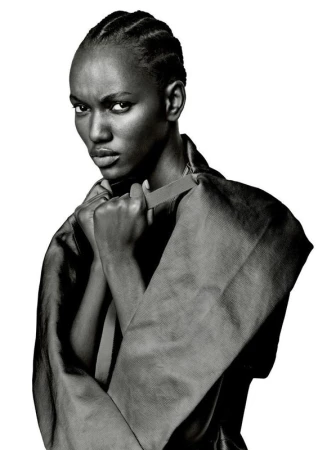 Black-and-white portrait of a woman with braided hair wearing a dark structured garment against a white background