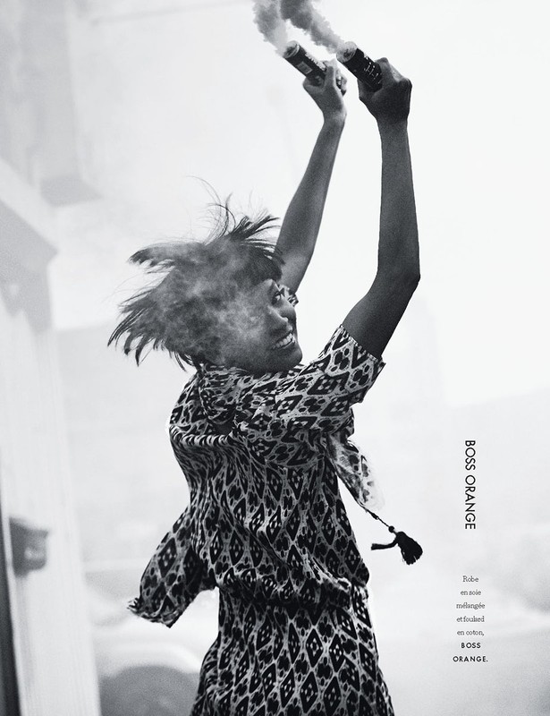 Monochrome fashion shot: a person in patterned dress holds smoking flares overhead, hair tousled, creating a dynamic, smoky fashion visual.
