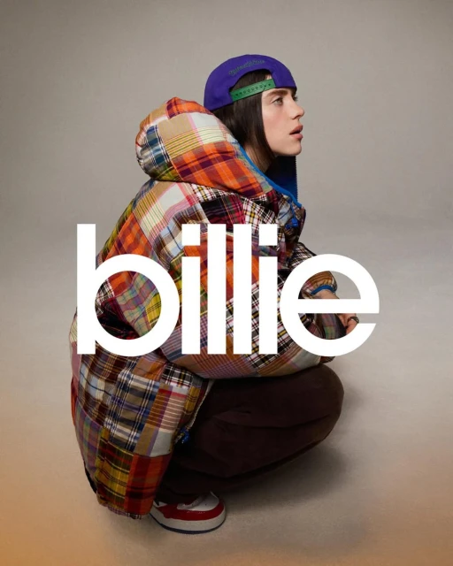 Portrait of a young adult in a colorful patterned coat and purple baseball cap, squatting against a neutral background with a serious expression.