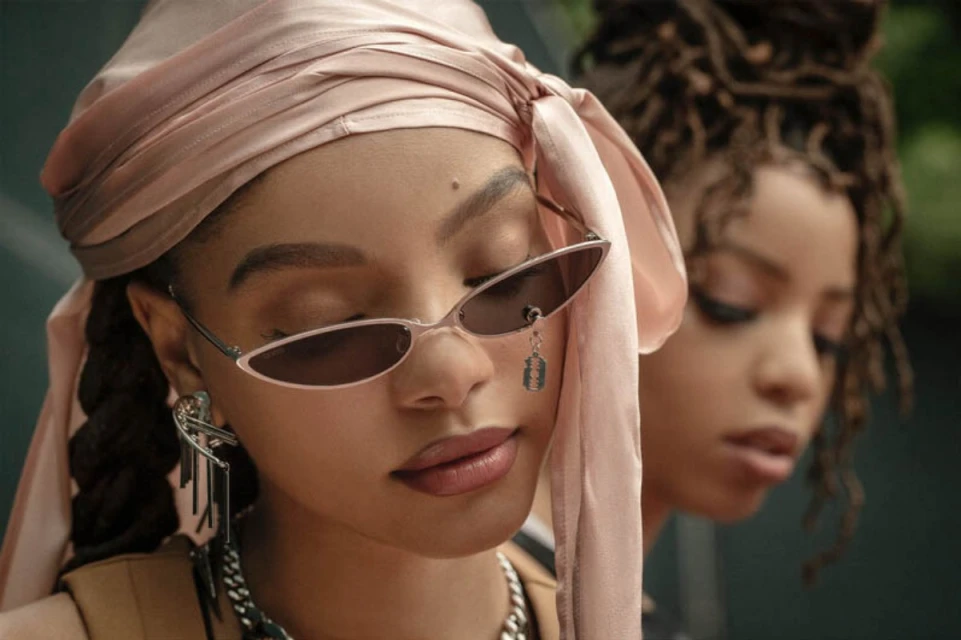 Close-up of two African-descent women with fair complexions, one in a headscarf and sunglasses, the other with natural curly hair.