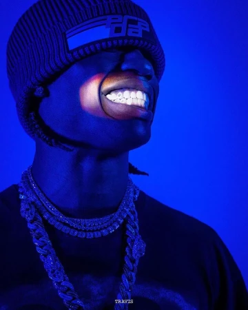 Close-up portrait of a man wearing a knit beanie and layered chain necklaces under dramatic blue lighting.