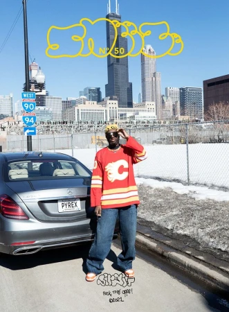 Man in sports jersey poses near car in urban setting with Chicago skyline and overcast sky in the background on a sunny day.