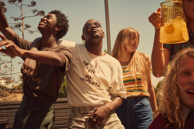 Group of diverse young adults outdoors with a drink pitcher, captured in warm, natural lighting with a shallow depth of field. Fashion and lifestyle.