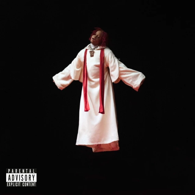 Young man in white robe with red trim against black background. Fashion-forward religious symbolism, unique style, bold visual statement.