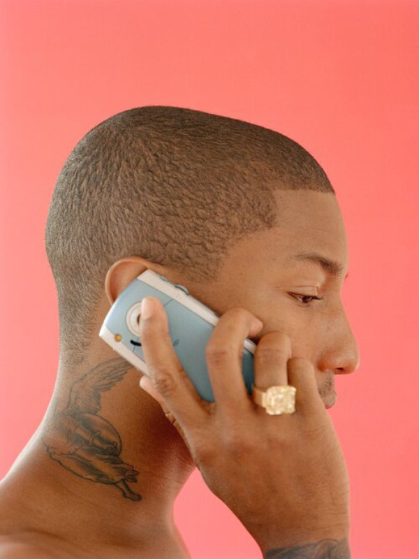 Side-profile portrait of a Black man talking on an older cellular phone against a coral background, focusing on his face, hand, and device.