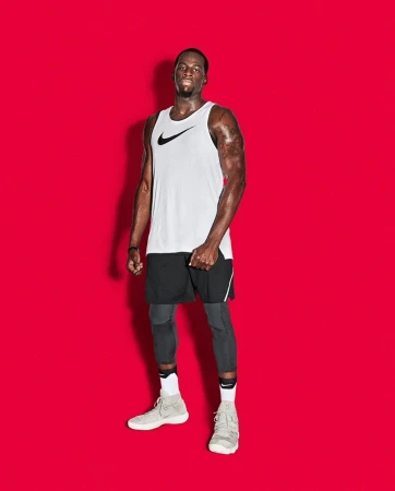 Athletic black man wearing white tank top and black shorts against a solid red studio background