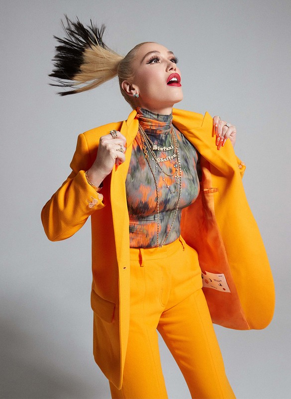 A fashionable young adult woman in a bright yellow suit with eye-catching hair, striking a pose in a studio setting, showcasing modern apparel.