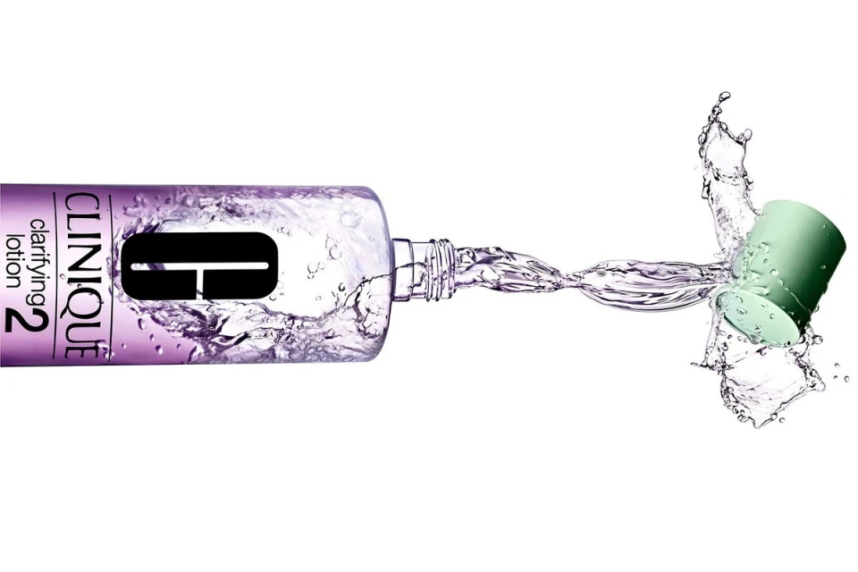 Clinique clarifying lotion bottle lying horizontally with cap off and liquid splashing. Product shot on a white background.